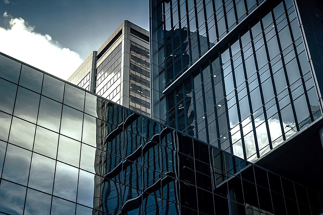 Glazed office towers whose curtain walls reflect sky and cloud